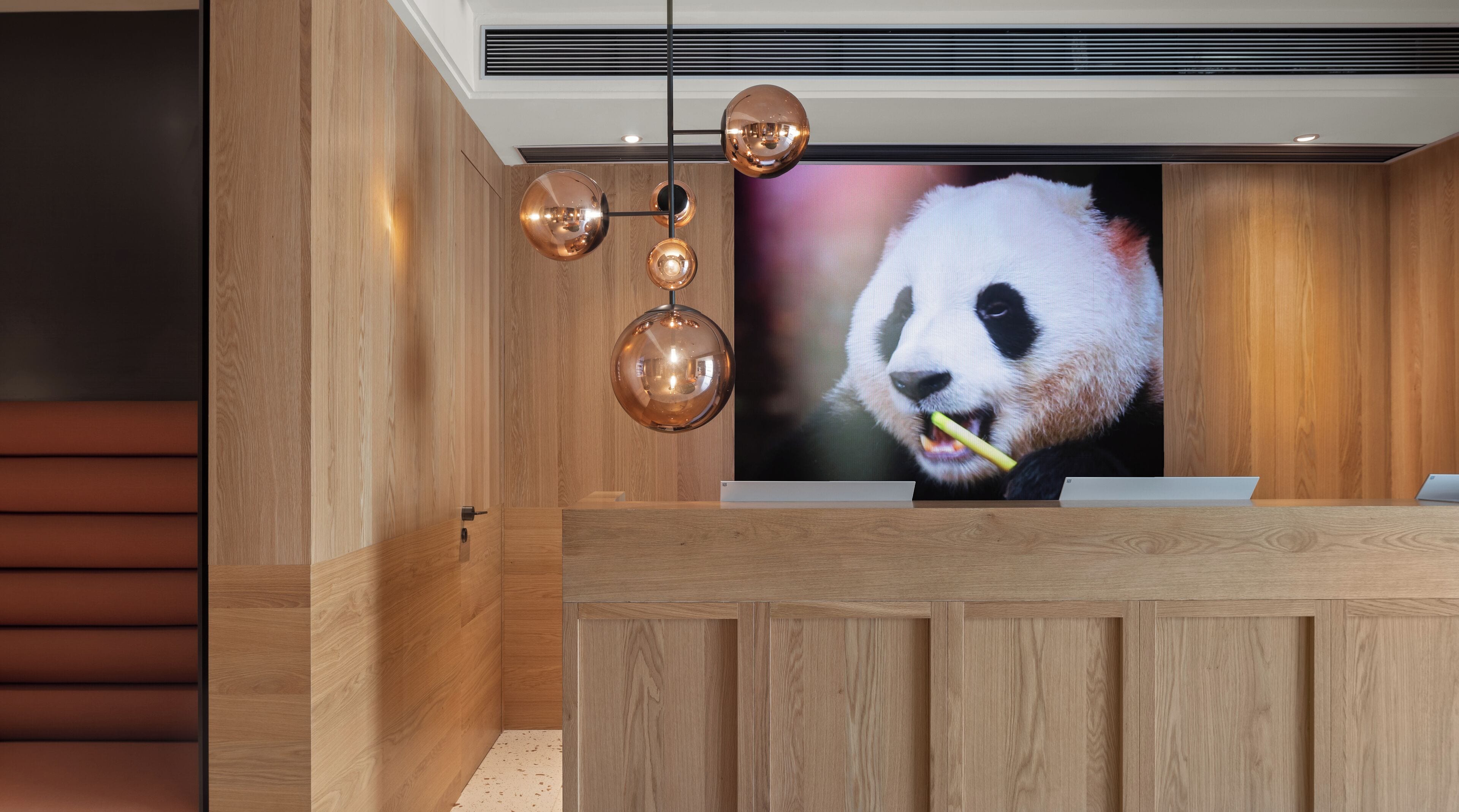 A reception area with a wooden reception desk, a large panda-themed TV screen, and a modern pendant light fixture.
