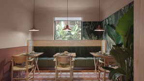 Interior de un restaurante con un banco acolchado verde, sillas de madera y un amplio ventanal con vistas a zonas verdes.