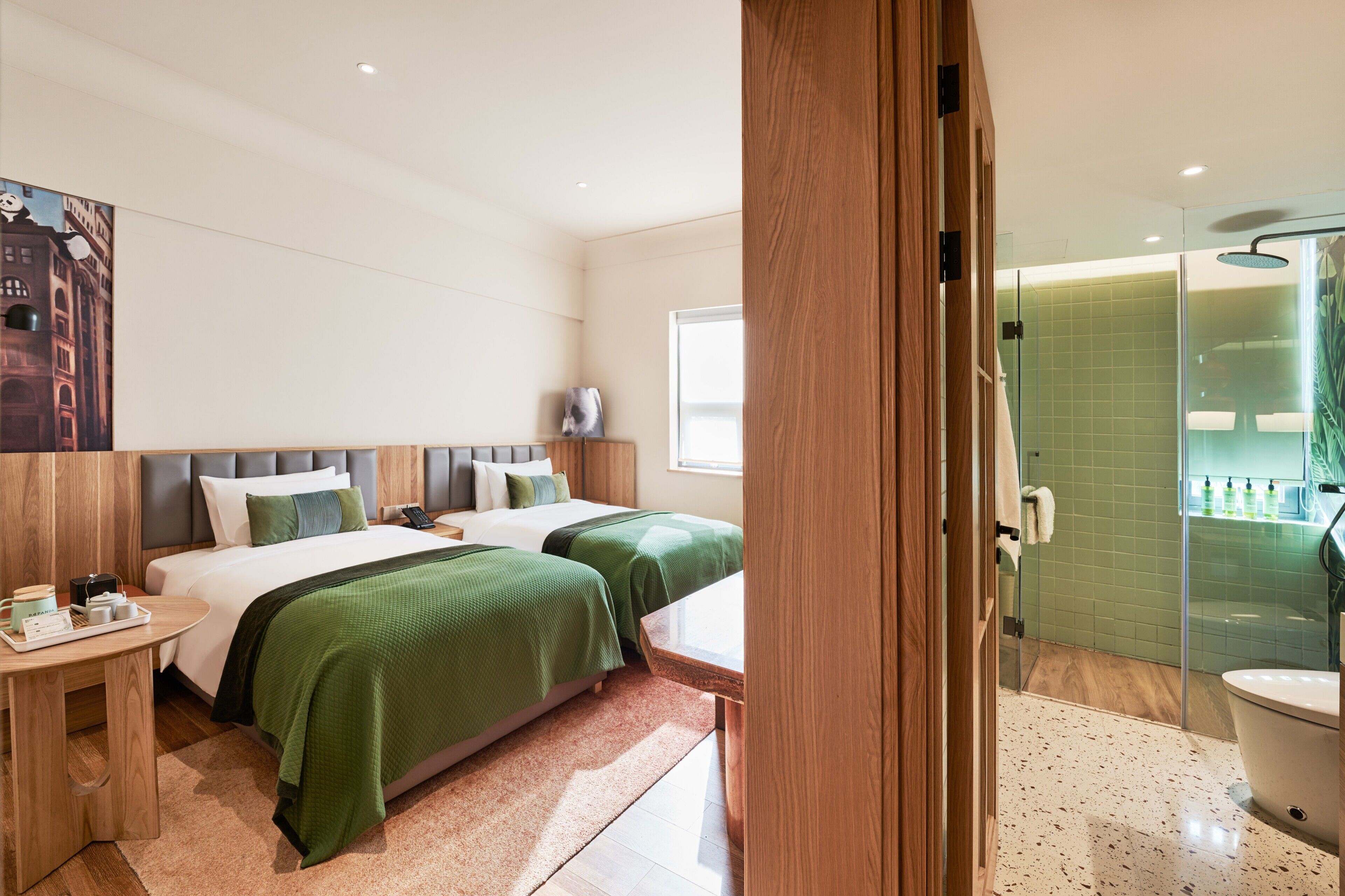 A hotel room with two beds, a bedside table, a nightstand, a window, and a shower area.