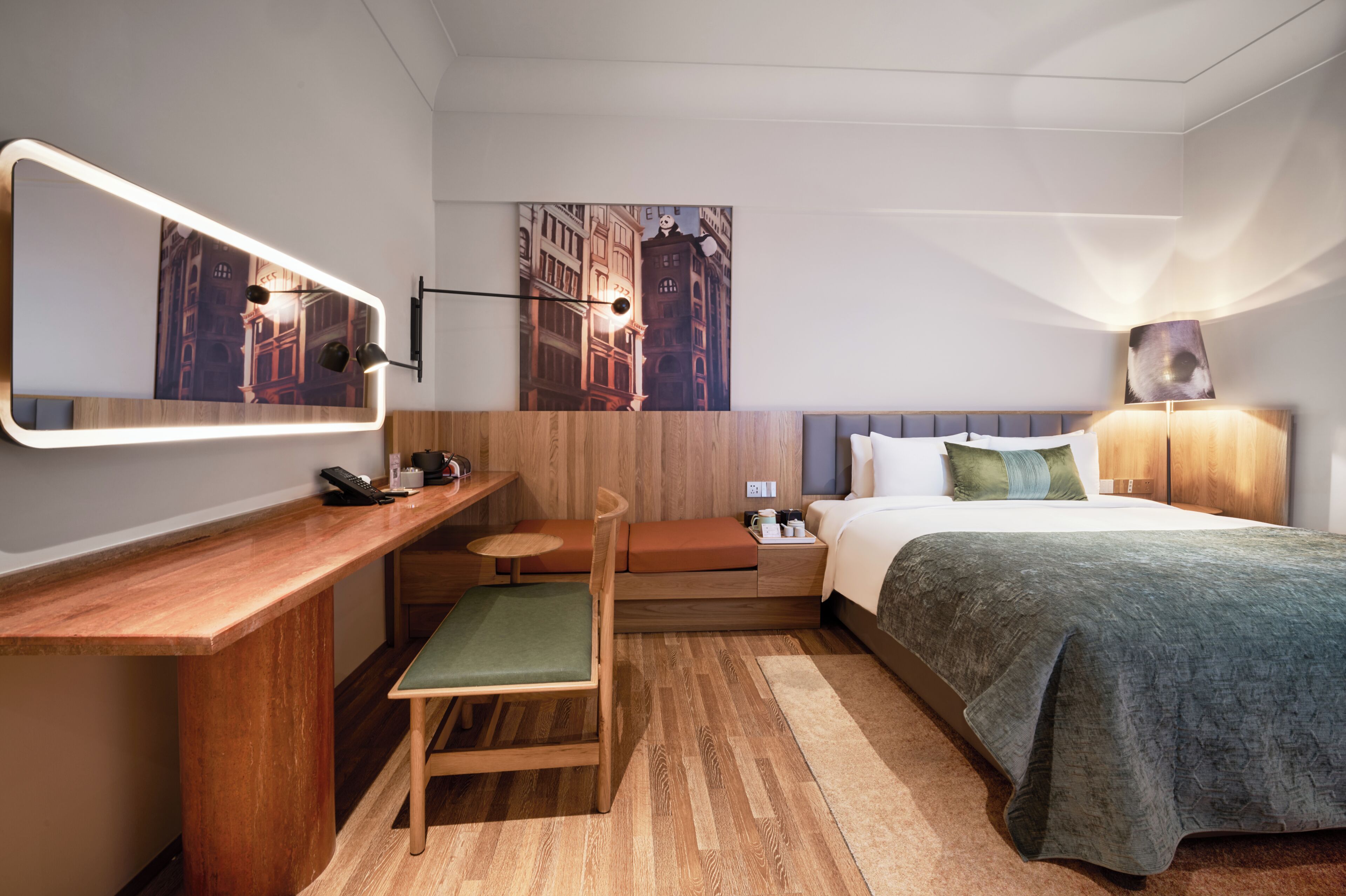 Habitación de hotel con cama, escritorio, silla, mesita de noche, lámpara y espejo en la pared.