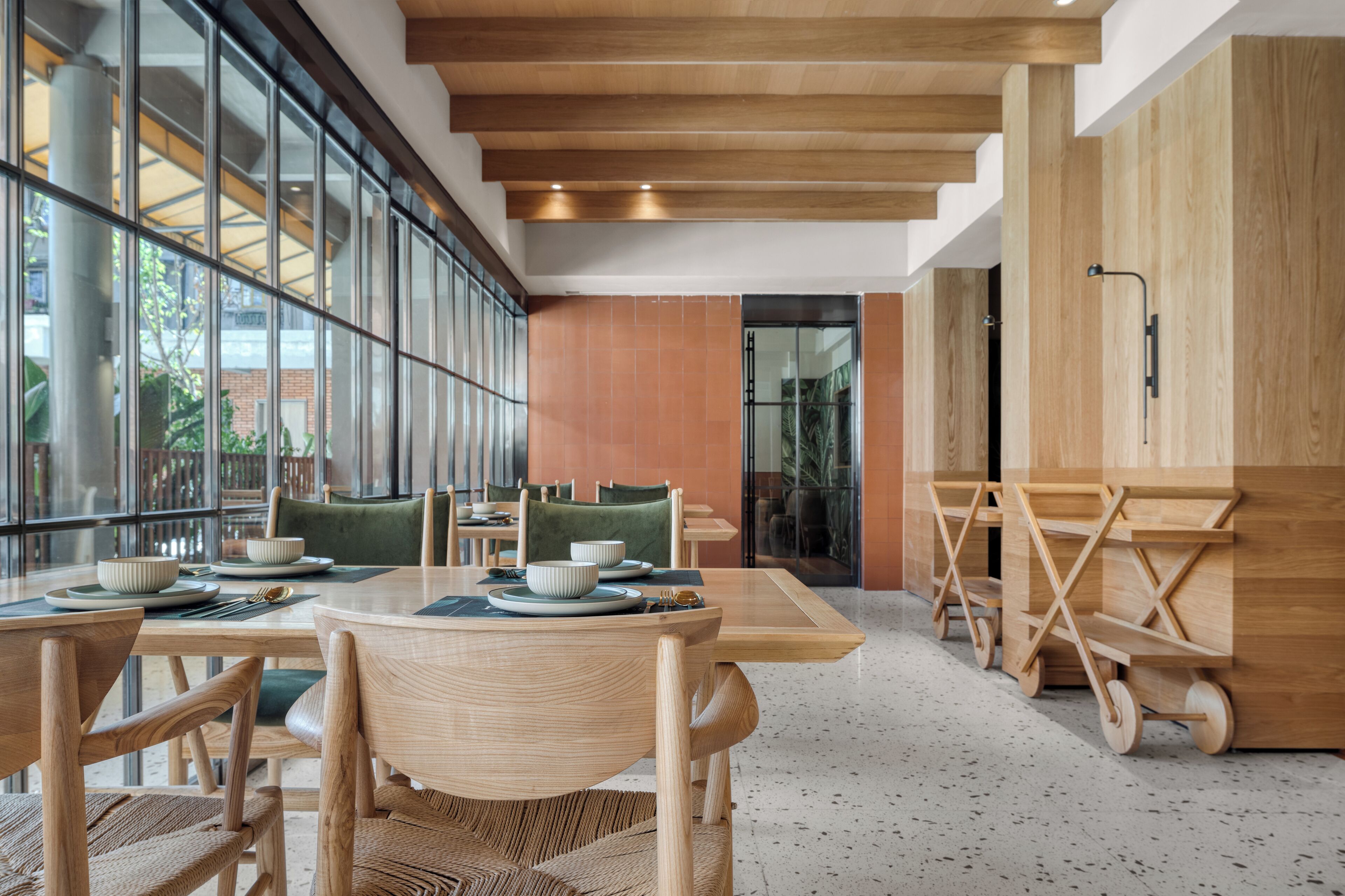 A modern dining area with wooden tables and chairs, large windows, and a view of the outdoors.