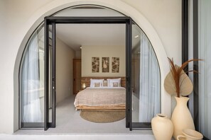 Ein Schlafzimmer mit einem großen Bett, einem Holz-Kopfteil und Blick durch einen Rundbogen.