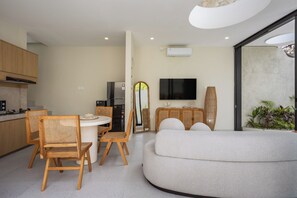 Eine moderne Küche mit Holzausstattung, ein Essbereich mit Korbstühlen, ein weißes Sofa und ein flachbildfernseher an der Wand.