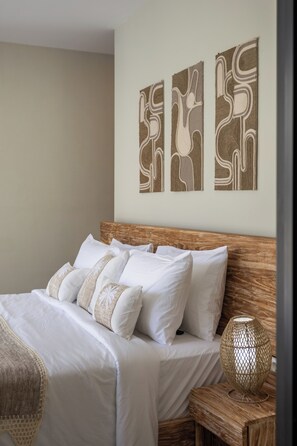 A neatly made bed with white linens and a wooden headboard, accompanied by a woven lamp on a wooden nightstand.