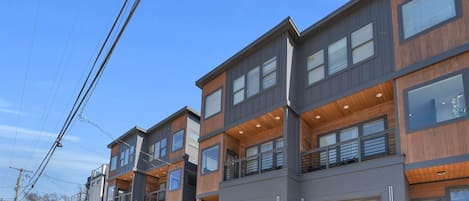 Un moderno edificio residencial de varios pisos, con garaje, balcones y cielo despejado.