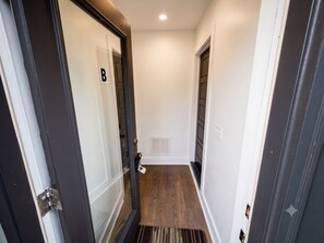 A narrow hallway with a wooden floor, a door with a 'B' sign, and a white wall with a vent. - Nashville Getaway • 1BR • King Bed • Private Entry (Nashville)