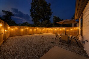 Een terras buiten, met een houten hek, lichtjes en een tafel met stoelen.