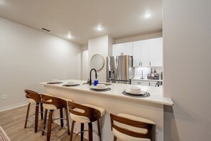 A modern kitchen with a central island, bar stools, stainless steel appliances, and white cabinetry. - Brand New 2BR/2BA - Less than .5 mile to Hospitals - Near Downtown (Tyler)