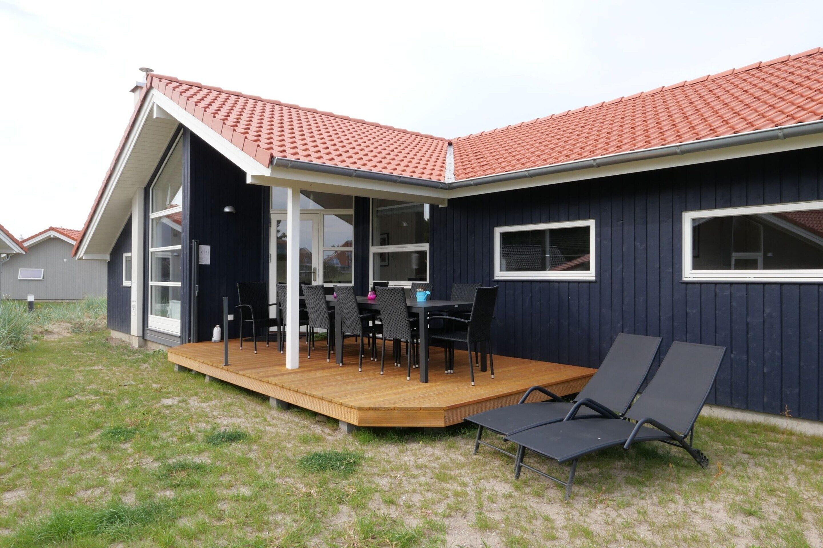Een modern huis met een overdekt terras, een eethoek met stoelen en een tafel, en een terras met ligstoelen.