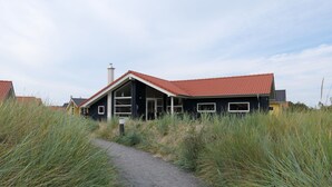 A modern house with a red-tiled roof, a pathway leading to the entrance, and surrounding tall grass. - Skandinavisches Haus fur 10 (Grossenbrode)