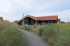 A modern house with a red-tiled roof, a pathway leading to the entrance, and surrounding tall grass. - Skandinavisches Haus fur 10 (Grossenbrode)