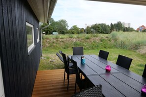 An outdoor dining area with a table and chairs, a view of the surrounding landscape, and a building with a dark exterior. - Skandinavisches Haus fur 10 (Grossenbrode)