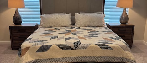 Une chambre à coucher comprenant un lit, deux tables de chevet, un banc et trois fenêtres équipées de stores.