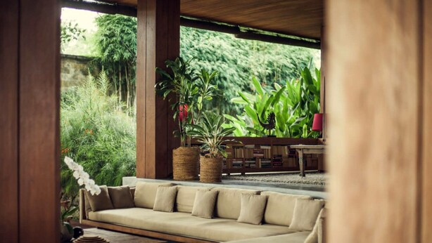 A cozy outdoor seating area with a sofa and a table, surrounded by lush greenery and a wooden pergola. - Red Garden Villa Pererenan (Badung)