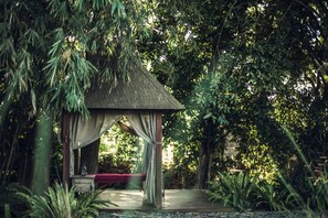 A gazebo with a thatched roof, surrounded by dense foliage and a wooden deck. - Red Garden Villa Pererenan (Badung)