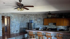 A kitchen with a stone wall, wooden cabinets, a bar area with stools, and a dining table with chairs.