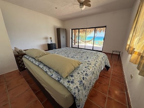 Un dormitorio con una cama grande, una mesita de noche, un armario y vistas al océano a través de una ventana.