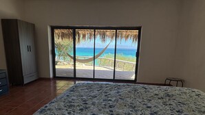 A bedroom with a bed, a wardrobe, a window with a view of the beach and ocean.