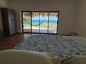 A bedroom with a bed, a wardrobe, a window with a view of the beach and ocean.