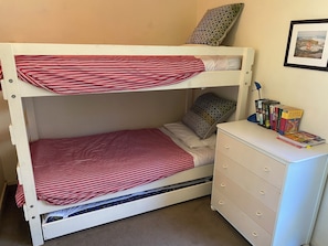 A bunk bed with a red and white striped bedspread, a pillow with a geometric pattern, and a small bedside table with a drawer. - COSY PORTSEA COTTAGE (Melbourne)