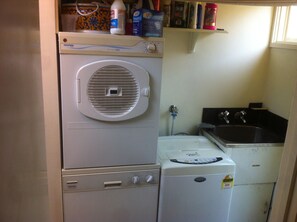 A compact laundry area with a front-loading washer, a dryer, and a sink. - COSY PORTSEA COTTAGE (Melbourne)