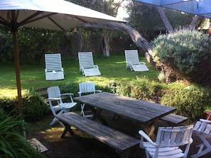 An outdoor patio with a wooden table and chairs, surrounded by greenery and a tree. - COSY PORTSEA COTTAGE (Melbourne)