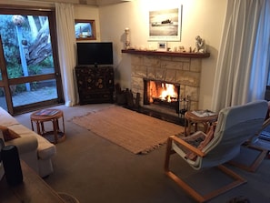 A cozy living room with a fireplace, a television, and a view through a large window. - COSY PORTSEA COTTAGE (Melbourne)