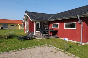 A red building with a covered patio, outdoor seating, and a gravel driveway.