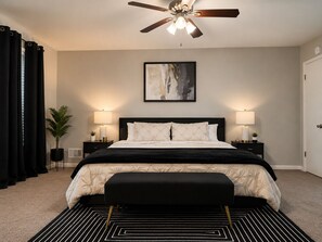 A bedroom with a bed, two bedside tables, a ceiling fan, a painting, and a black and white patterned rug. - 3-bedroom house in Atlanta 13min from Airport (Ellenwood)