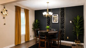 Un'area pranzo con un tavolo rotondo, sedie, un lampadario e una parete con motivi geometrici.