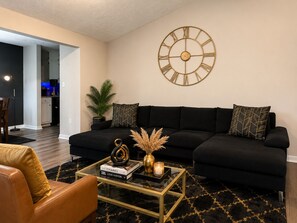 Ein Wohnzimmer mit einem schwarzen Sofa, einem Couchtisch und einer großen Wanduhr.