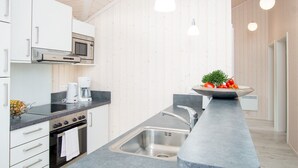A modern kitchen with white cabinetry, a built-in microwave, a coffee maker, and a sink with a contemporary faucet. - Grobenbrode Green Lawn Sanctuary (Grossenbrode)