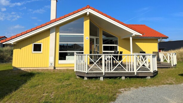 A yellow building with a red roof, a chimney, and a balcony with white railings. - Spa-cottage mit Rampe (Grossenbrode)