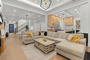 A spacious living room with a large sectional sofa, a wooden coffee table, and a staircase leading to another level. - Large Luxury New Modern home w/ Patio/AC/Bar (Delta)