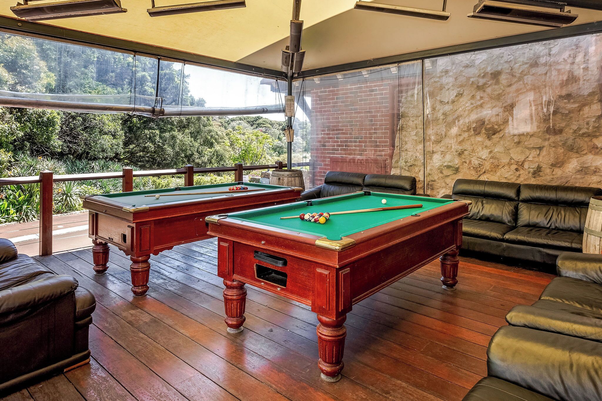 A pool table with two adjacent seating areas, a wooden floor, and a view of greenery outside.