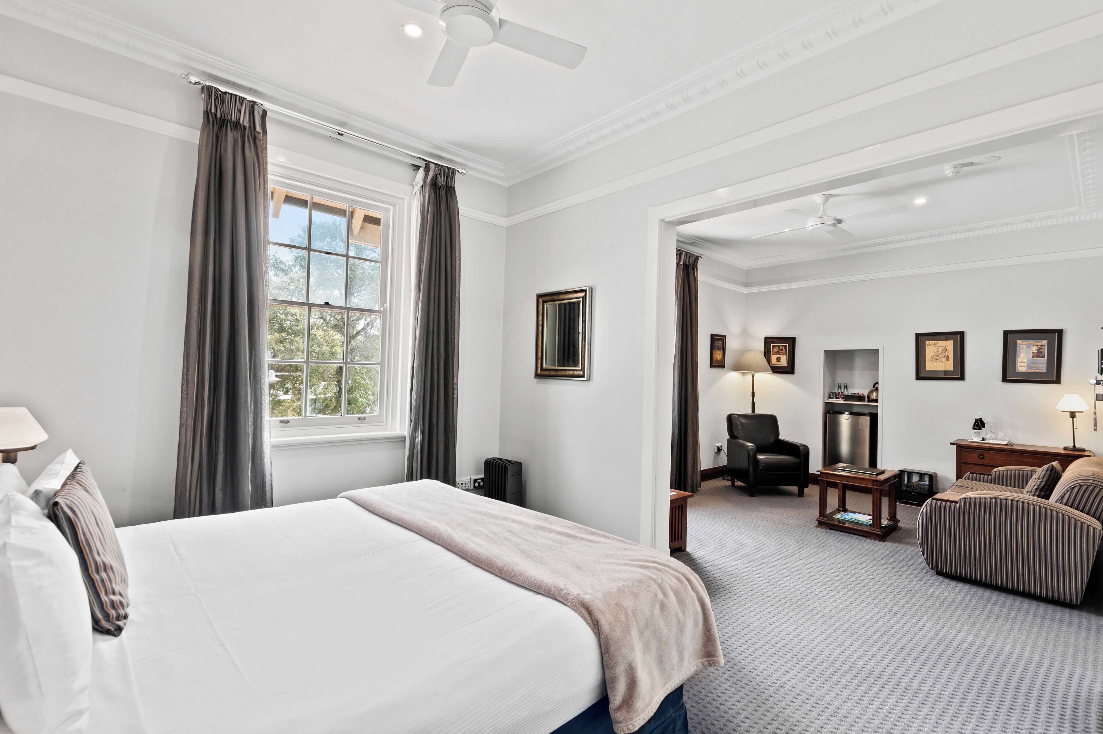 A hotel room with a bed, a desk, a chair, a sofa, a radiator, and a window with curtains.