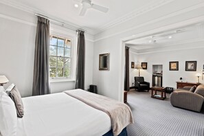 A hotel room with a bed, a desk, a chair, a sofa, a radiator, and a window with curtains.
