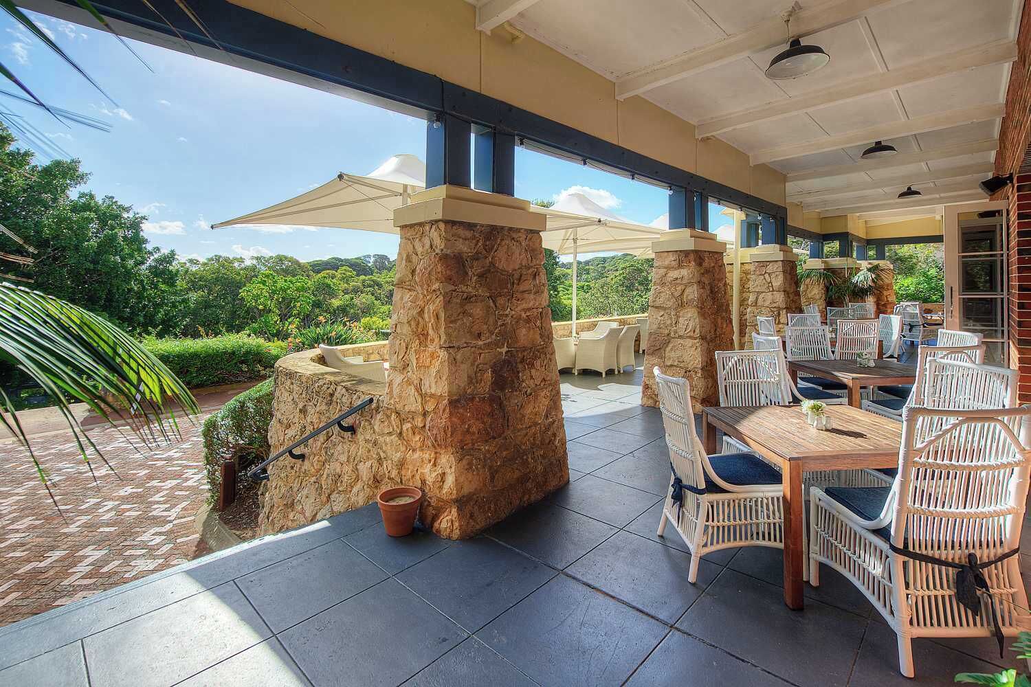 An outdoor patio with stone pillars, white wicker furniture, and umbrellas.