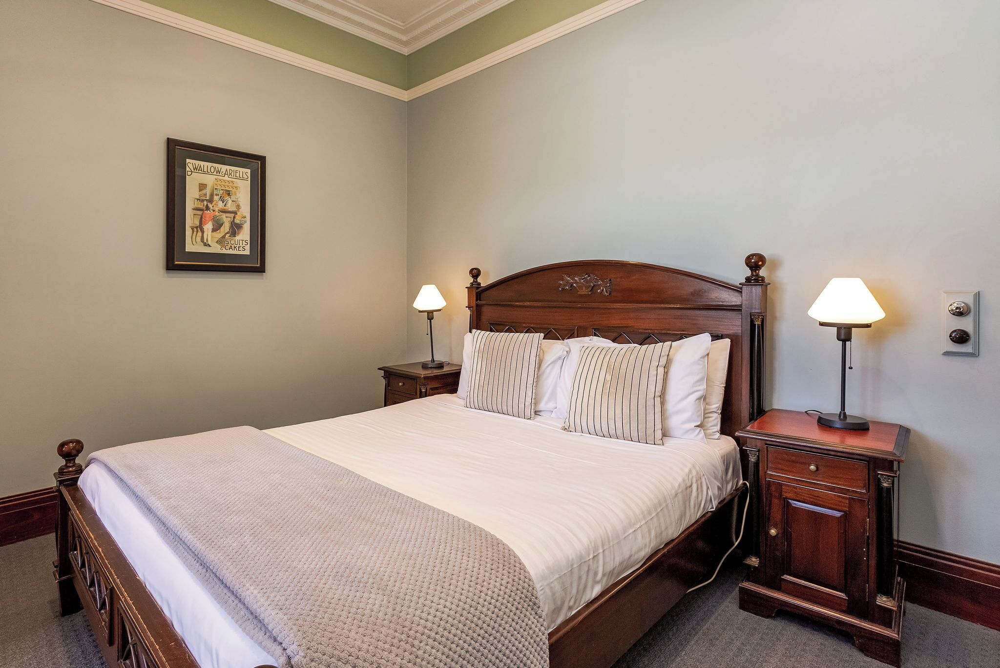 A neatly made bed with a wooden headboard, two bedside tables with lamps, and a framed picture on the wall.