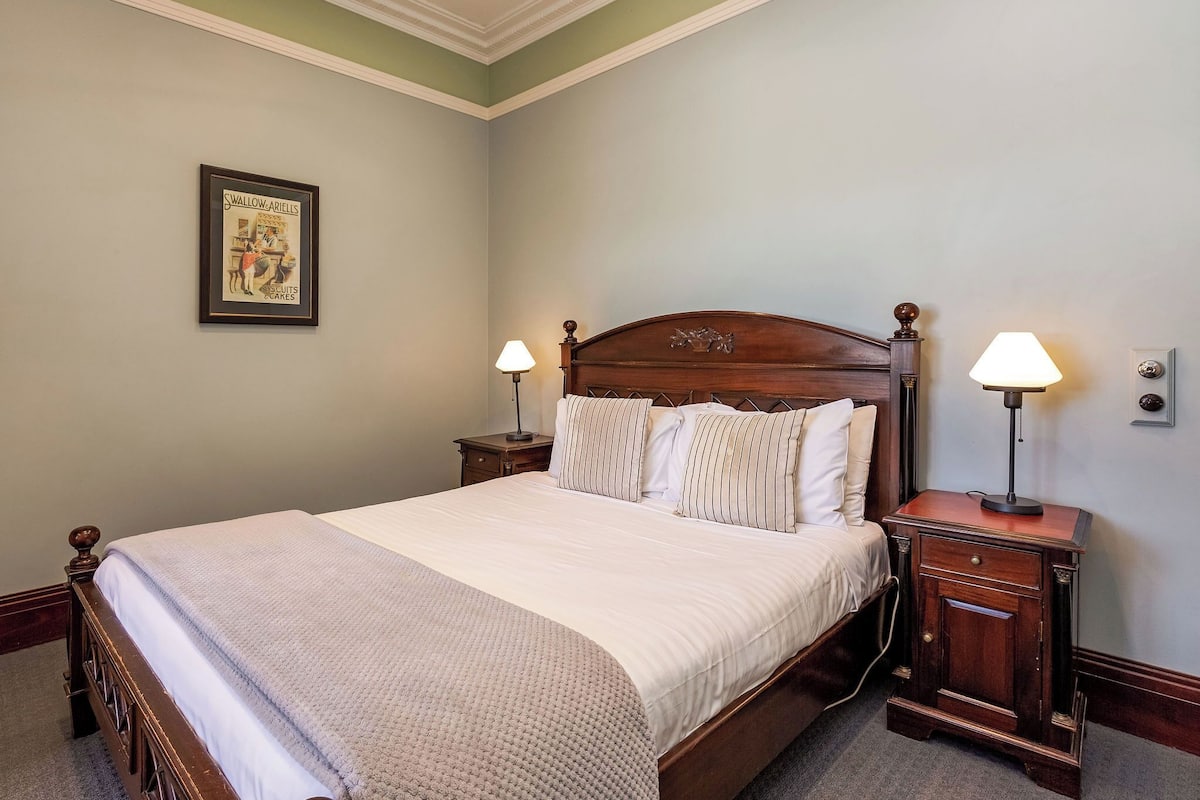 A neatly made bed with a wooden headboard, two bedside tables with lamps, and a framed picture on the wall.