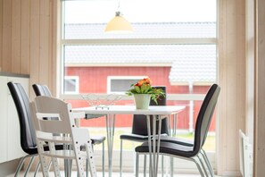 Ein Essbereich mit Tisch und Stühlen, ein Blumentopf mit Blumen und Blick auf ein rotes Gebäude.