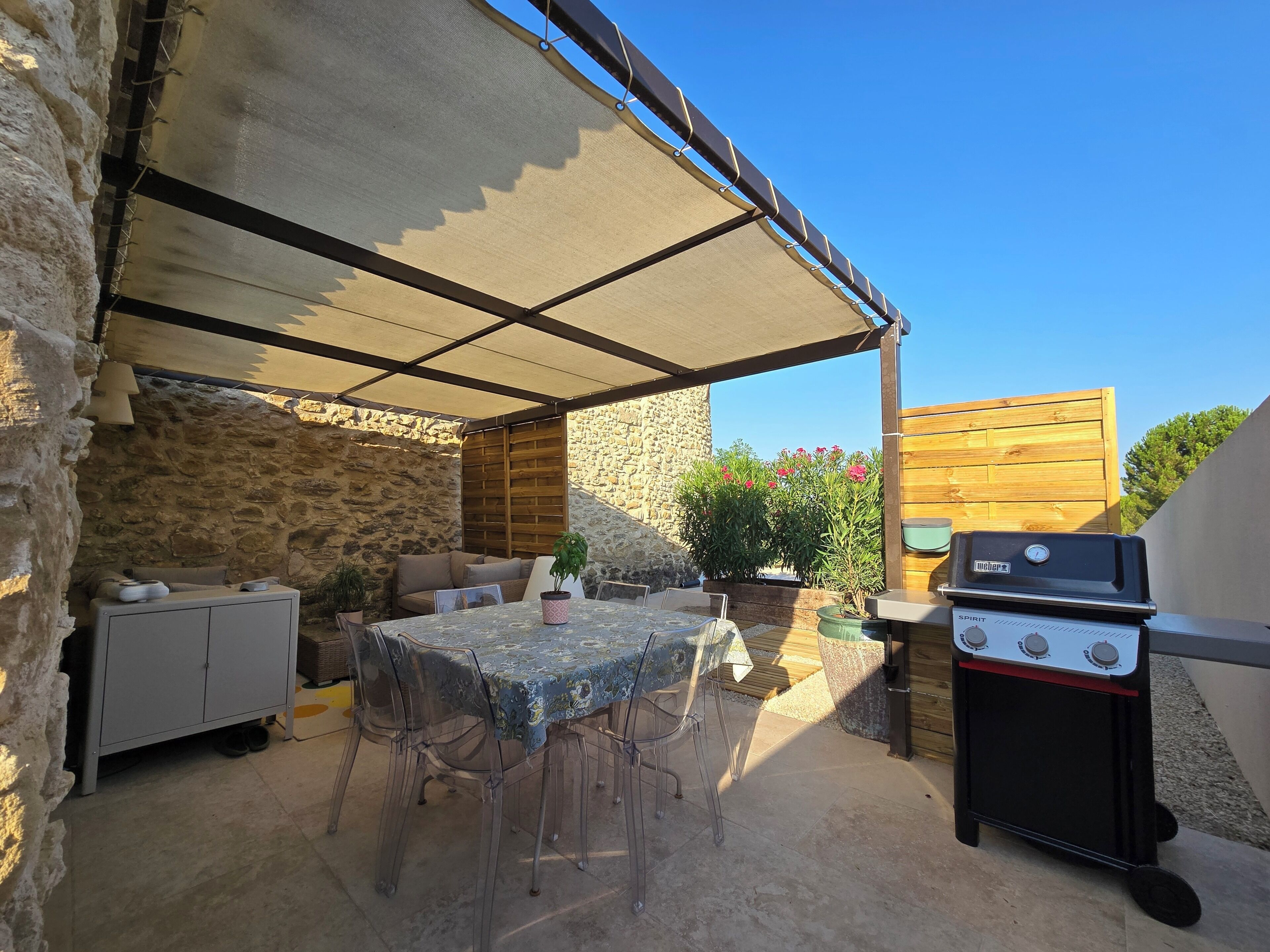 Eine Terrasse im Freien mit Tisch, Stühlen, einem Grill und einer Steinmauer.