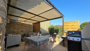 Un patio esterno con tavolo, sedie, barbecue e un muro in pietra.