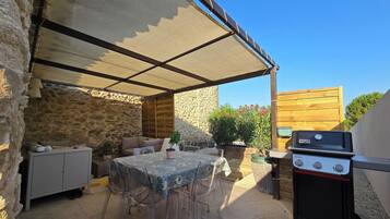 An outdoor patio with a table, chairs, a grill, and a stone wall.