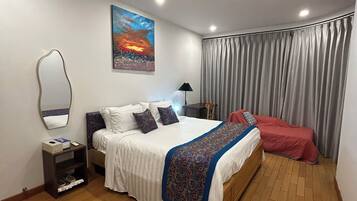 A bedroom with a bed, a nightstand, a lamp, a painting, and a window with curtains.