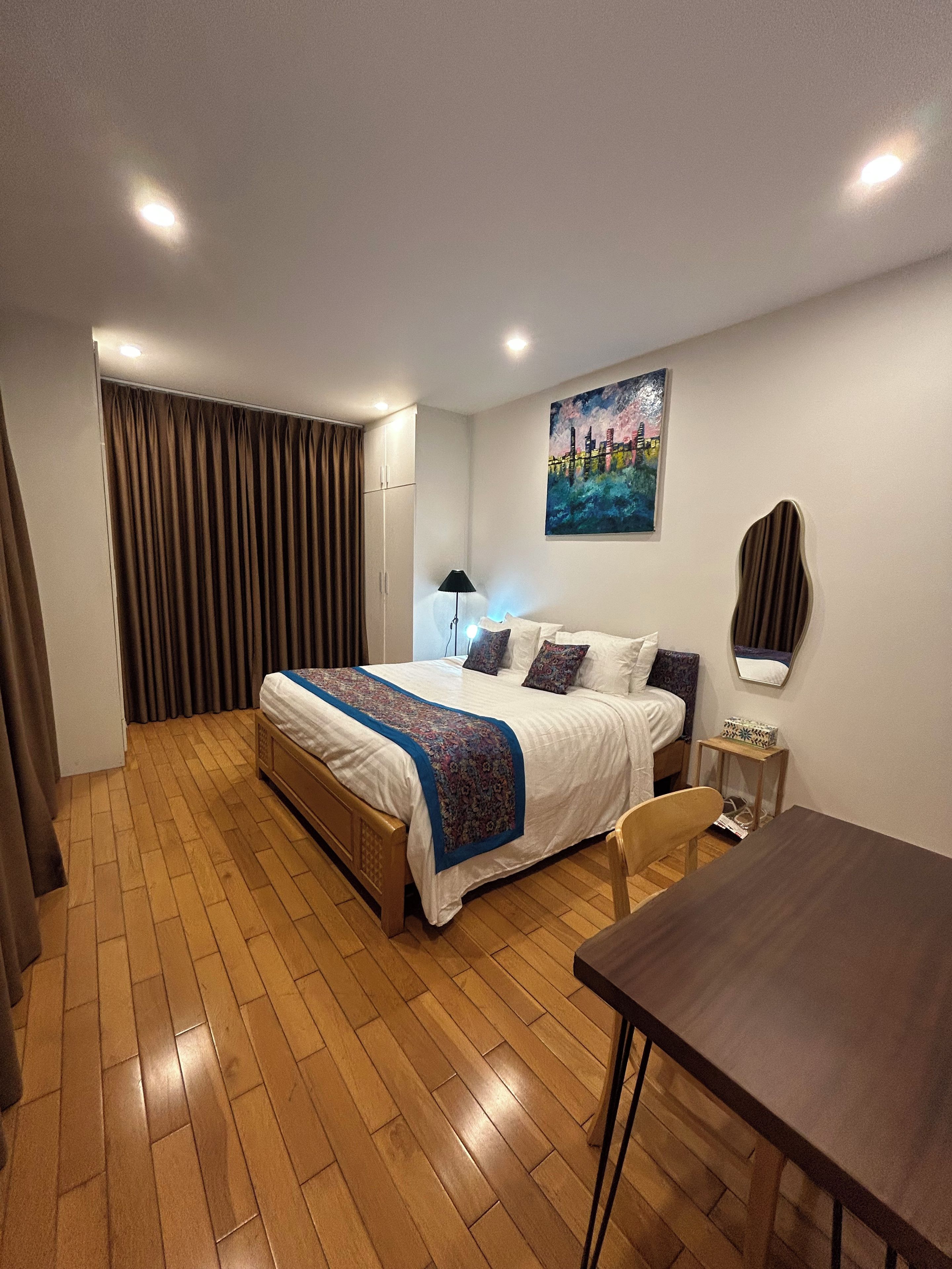 Una camera d'albergo con un letto, una scrivania, una sedia, una lampada, un quadro e una tenda.
