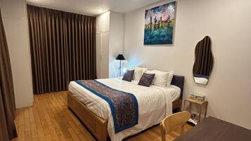 Una camera d'albergo con un letto, una scrivania, una sedia, una lampada, un quadro e una tenda.