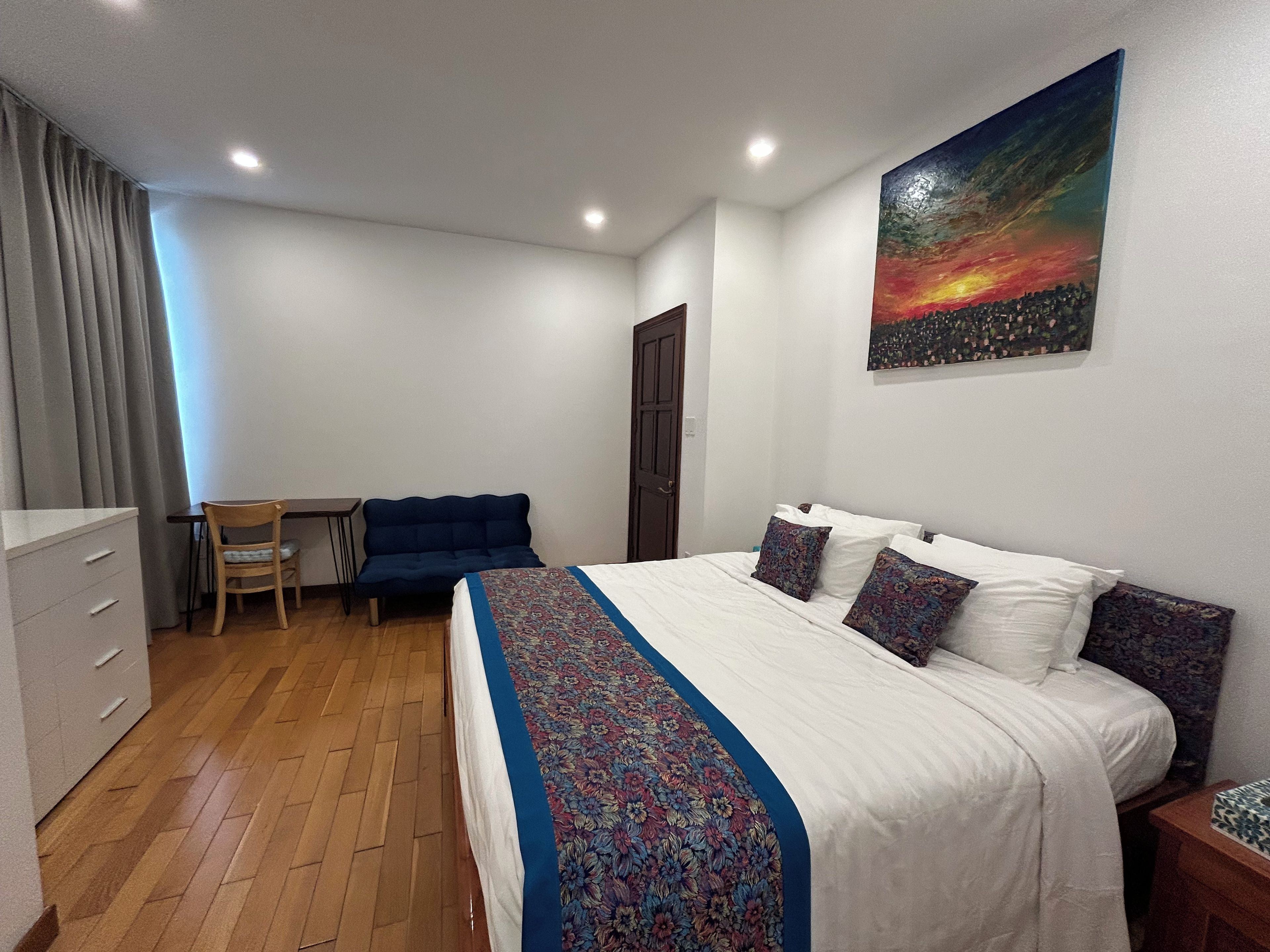 Een slaapkamer met een bed, een bureau, een stoel en een schilderij aan de muur.