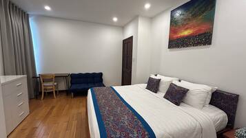 A bedroom with a bed, a desk, a chair, and a painting on the wall.