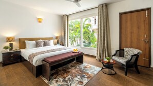 A bedroom with a bed, bedside tables, a bench, a chair, a ceiling fan, a window with curtains, and a view of greenery outside.